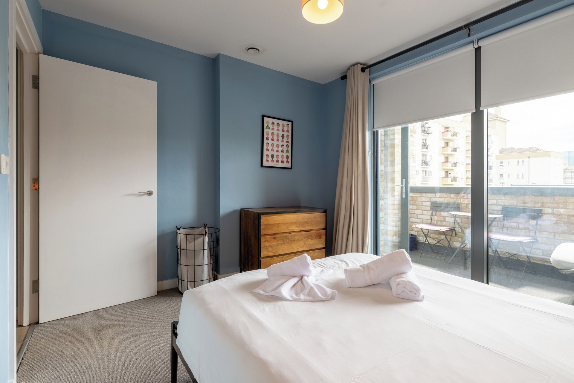 A hotel room with a bed, a dresser, a window with a view of buildings, and a door.