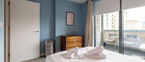 A hotel room with a bed, a dresser, a window with a view of buildings, and a door.