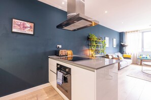 A modern kitchen with a built-in oven, a stainless steel range hood, and a small island with a toaster. - Contemporary East London Hideaway with Balcony (Greater London)