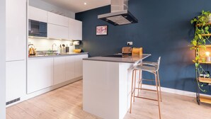A modern kitchen with white cabinets, a stainless steel range hood, and a wooden island with bar stools. - Contemporary East London Hideaway with Balcony (Greater London)
