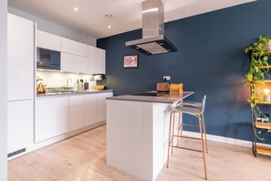 A modern kitchen with white cabinets, a stainless steel range hood, and a wooden island with bar stools. - Contemporary East London Hideaway with Balcony (Greater London)