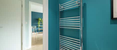Un pasillo con pared verde azulado, un perchero metálico y una puerta que da a otra habitación.