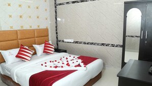 Una cama bien hecha con una colcha roja y blanca, dos almohadas y un arreglo de flores rojas en forma de corazón sobre la cama.