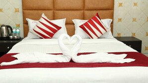 Una cama con cabecera marrón, ropa de cama blanca, almohadas a rayas rojas y blancas, y dos toallas blancas dispuestas en forma de corazón.