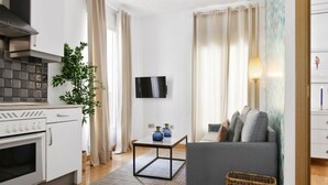 A modern living room with a sofa, a small table, a TV, and a kitchen area with an oven. - 8-guest Central Madrid Haven (Madrid)