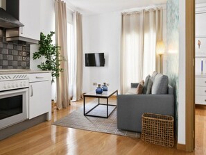 A modern living room with a sofa, a small table, a TV, and a kitchen area with an oven. - 8-guest Central Madrid Haven (Madrid)