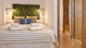 A neatly made bed with striped bedding, two rolled towels, and a green leafy wall decoration. - 8-guest Central Madrid Haven (Madrid)
