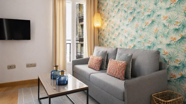 A living room with a grey sofa, patterned wallpaper, a flat-screen TV, a coffee table, and a window with curtains. - 8-guest Central Madrid Haven (Madrid)