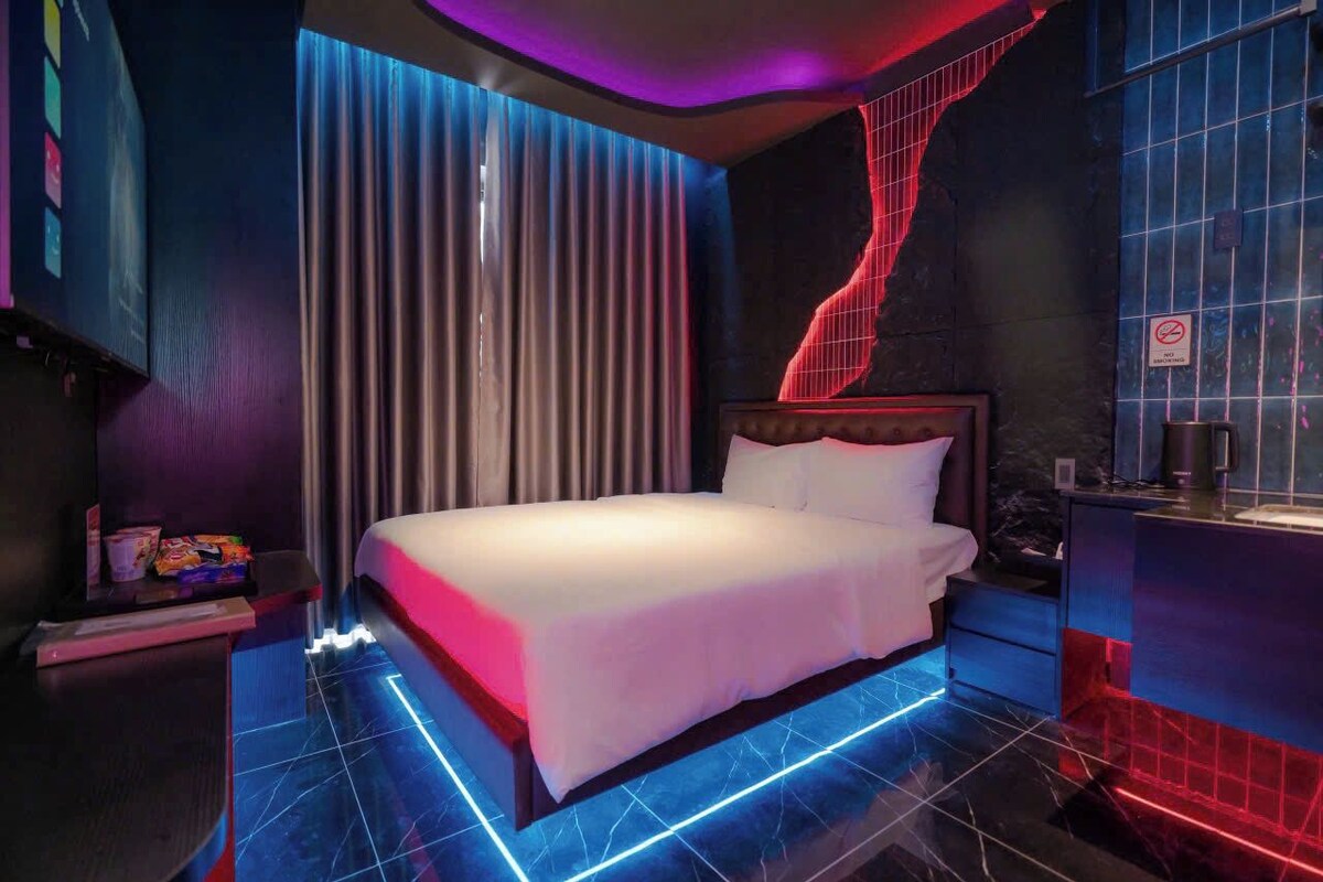 A modern hotel room with a bed, curtains, a nightstand, and a wall with a geometric light design.