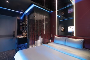 A modern hotel room with a bed, a vanity, and a shower area.
