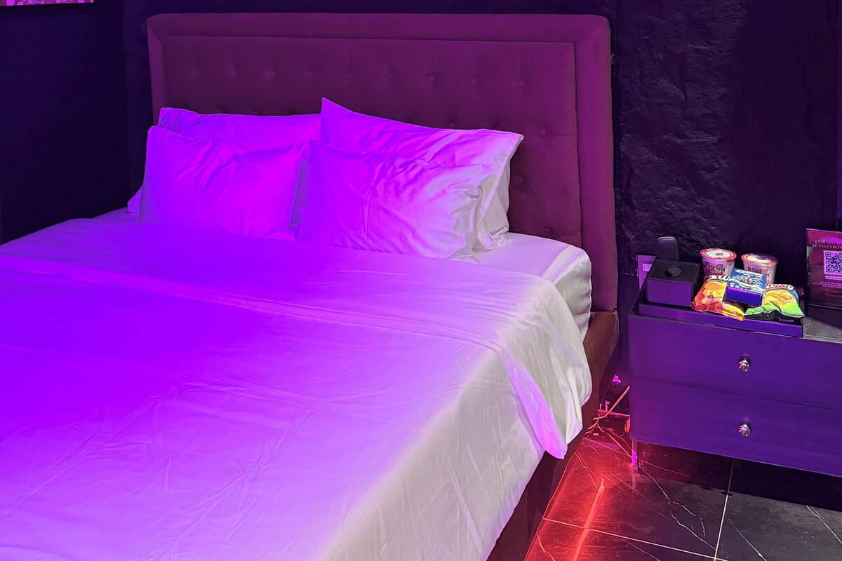 A bedroom with a bed, a projector mounted on the wall, and a nightstand with snacks.