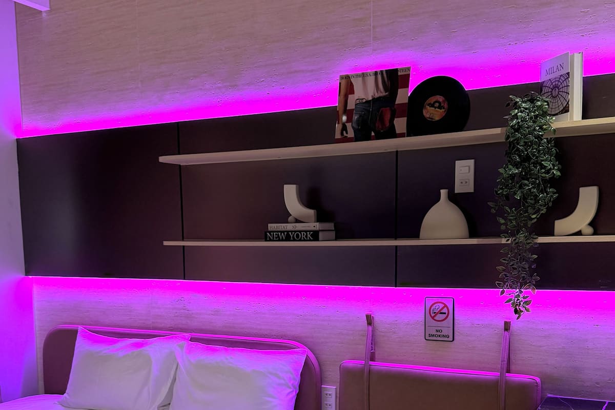 A modern bedroom with a bed, bedside table, and a shelf with books and decorative items.
