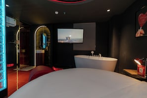 Een moderne hotelkamer met een groot bed, een aan de muur bevestigde televisie, een badkuip en een spiegel.