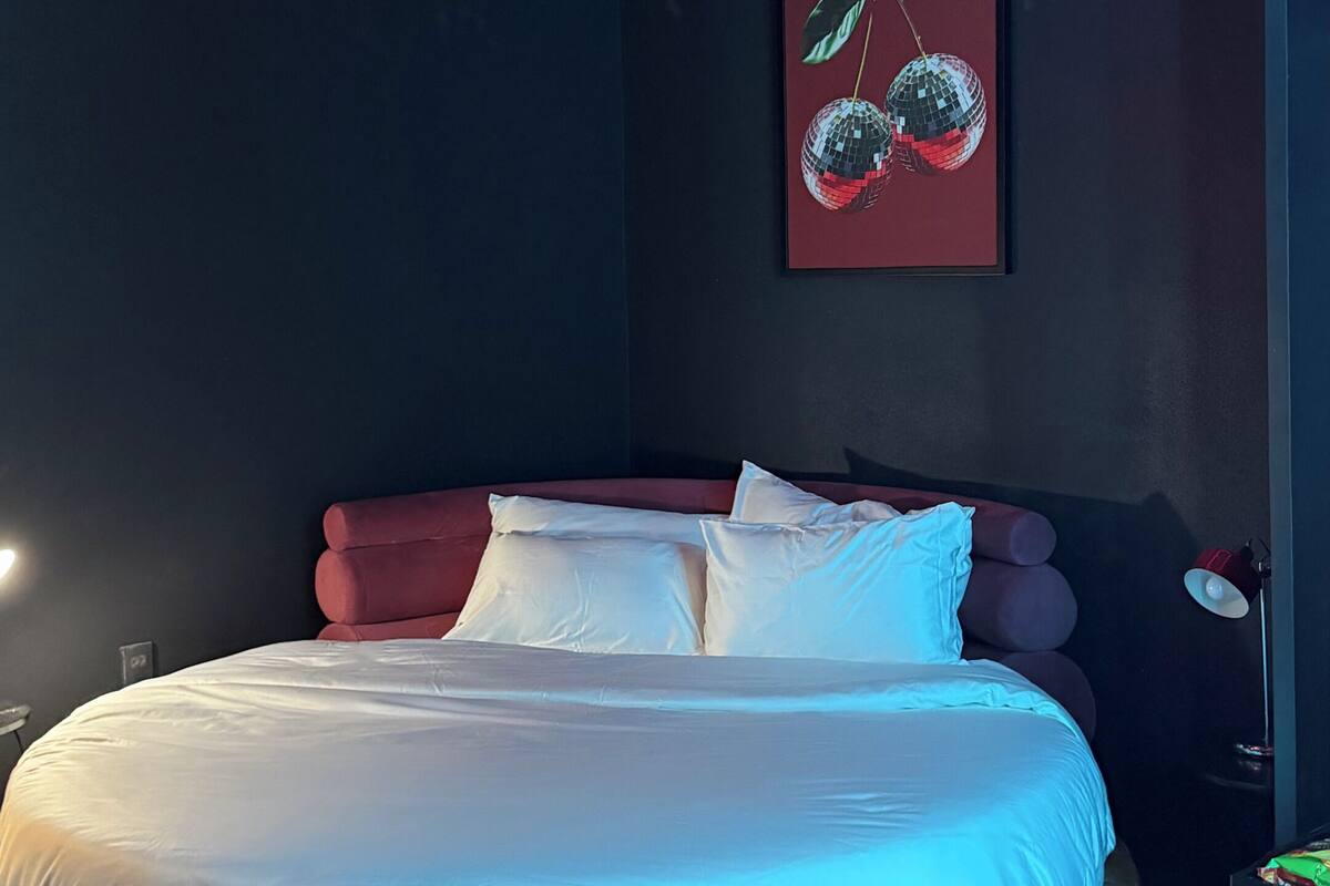 A modern bedroom with a curved ceiling, a bed with white linens, and two wall-mounted artworks.