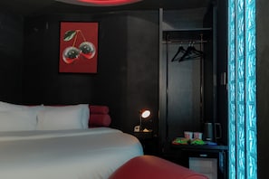 Een hotelkamer met een bed, een bureau met een lamp, een kapstok en een raam met gordijnen met een patroon.