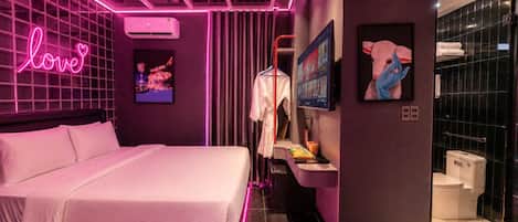 Ein modernes Schlafzimmer mit einem Bett, einem leuchtenden 'love'-Schild, einer Wand-Klimaanlage und einem durchgehenden Türspalt sichtbaren Badezimmer.