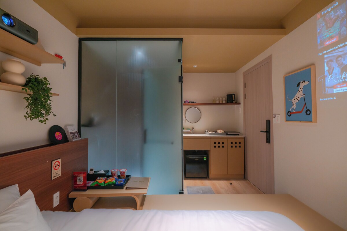 A hotel room with a bed, a desk, a small kitchenette, and a sliding door leading to a bathroom.