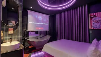 Een moderne hotelkamer met een groot bed, een rond bad, een kaptafel met spiegel en een televisiescherm waarop een menu wordt getoond.