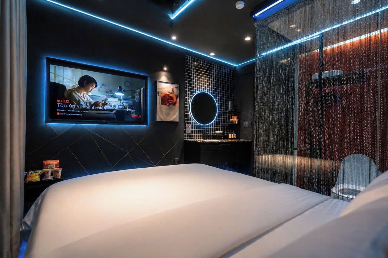 Une chambre d’hôtel moderne avec un grand lit, un téléviseur fixé au mur et un luminaire circulaire.