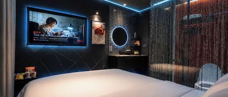 Une chambre d’hôtel moderne avec un grand lit, un téléviseur fixé au mur et un luminaire circulaire.