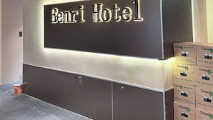 A reception area with a sign for 'Benri Hotel,' a tiled floor, and a stack of boxes on the right.