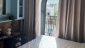 A hotel room with a bed, a TV mounted on the wall, a window with curtains, and a view of the outside.