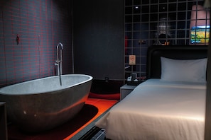 A modern bathroom with a large freestanding bathtub, a shower, and a bed with a headboard.