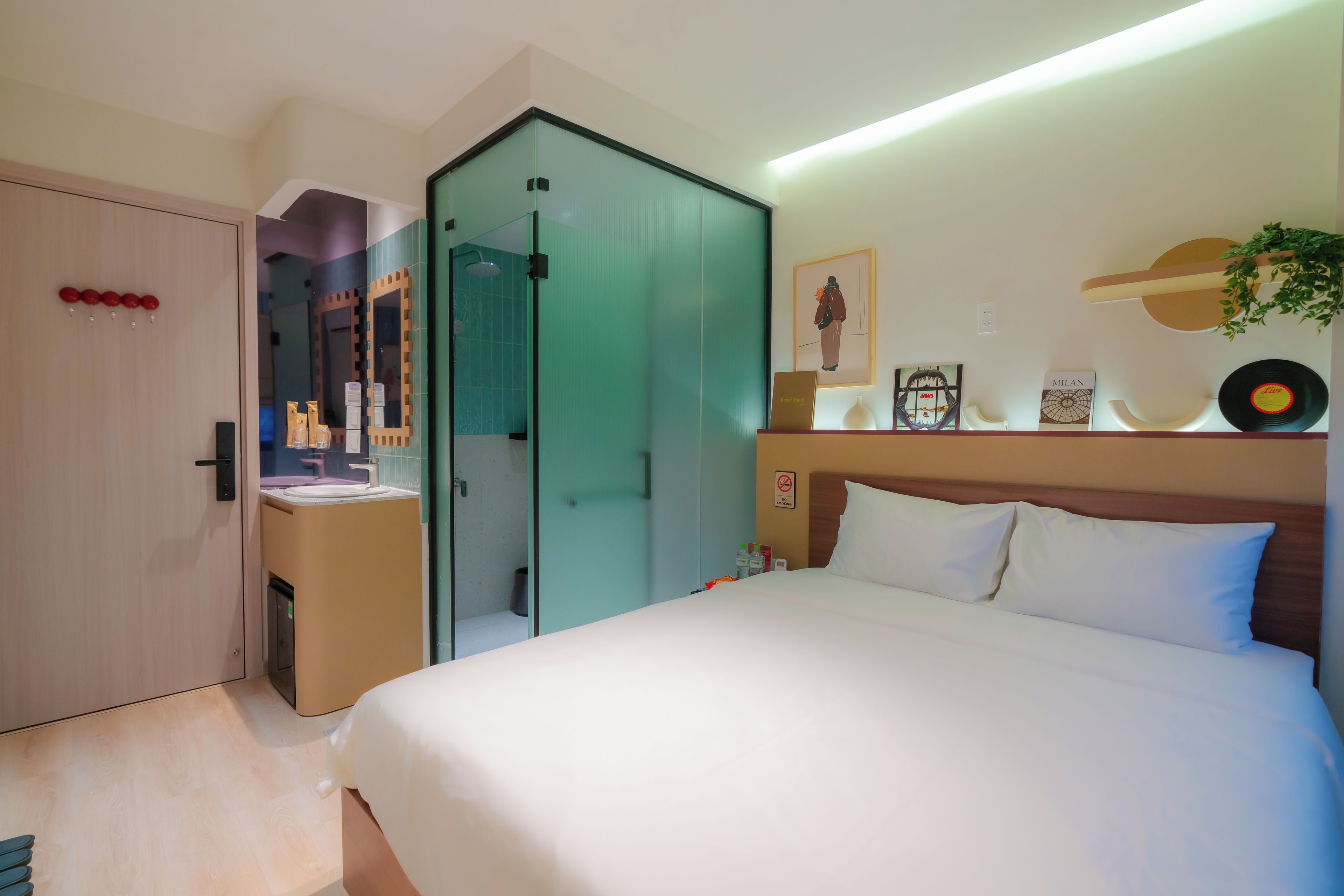 A hotel room with a bed, a shower area, a vanity with a mirror, and a wall with framed pictures and a record.