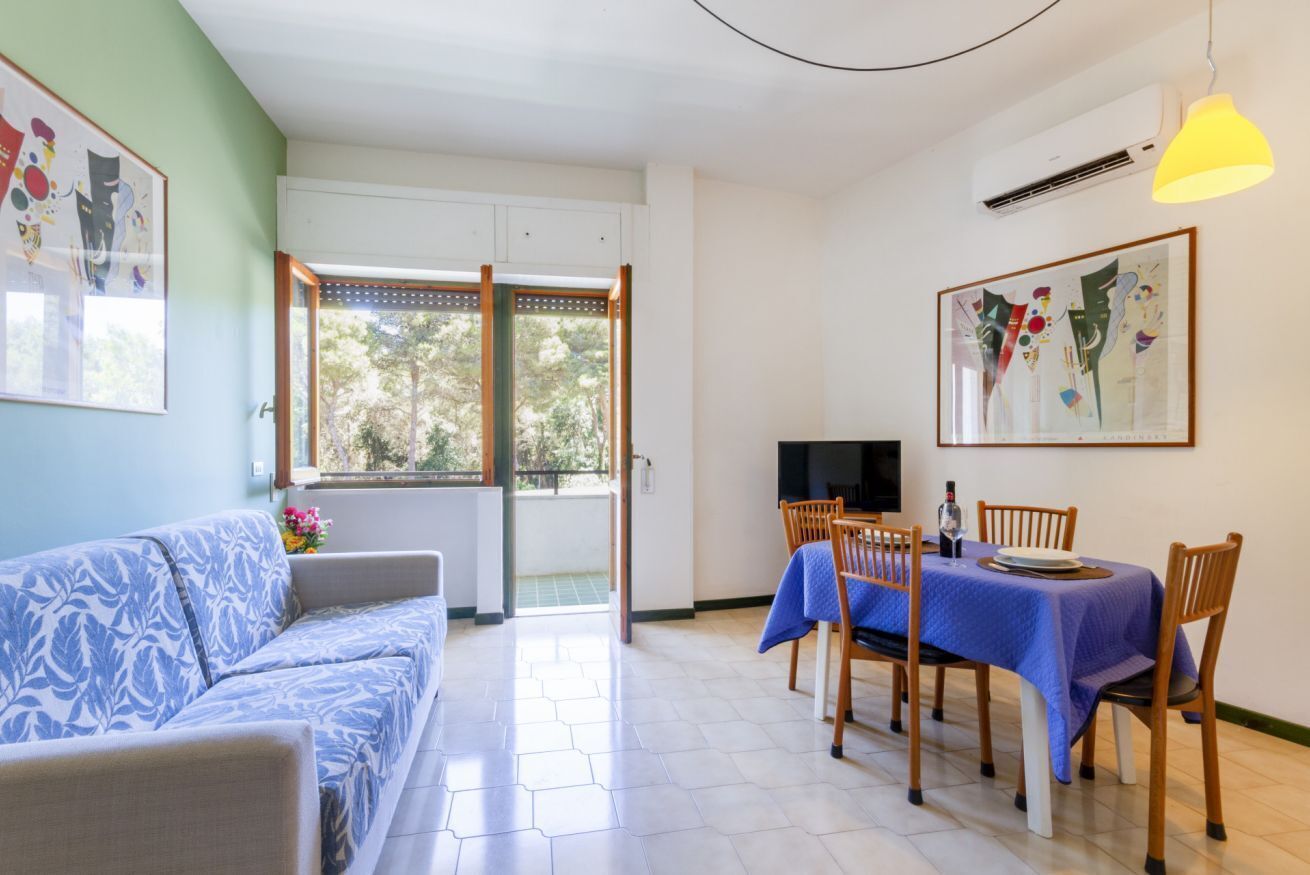 A living room with a sofa, dining table, chairs, a TV, and artwork on the walls.