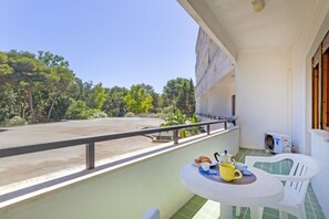 Ein Balkon mit Tisch, Stuhl und Blick auf einen Parkplatz und Bäume.