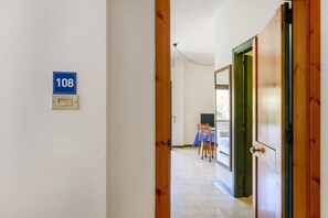 Ein Flur mit einer Tür mit der Aufschrift '108', ein Essbereich mit Tisch und Stühlen sowie ein Blick auf einen Balkon.