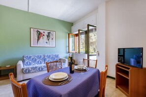A dining area with a table set for two, a sofa, and a television. - A cozy apartment with a balcony that sleeps up to four people, located within the Campoverde Residence in Vernole—set in a Mediterranean pine forest between San Cataldo and the Le Cesine State Nature Reserve. The property is just a short distance from  (Campo Verde)