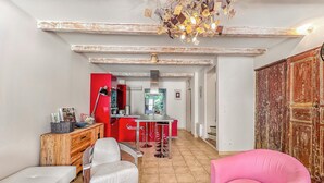A modern kitchen with a red accent wall, a dining area with a wooden table and white chairs, and a pink armchair.