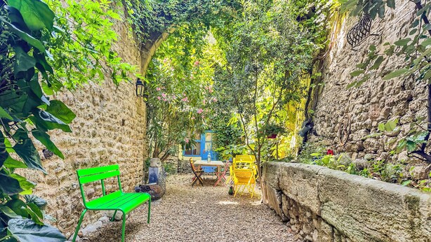 A stone wall, a green bench, and a yellow chair in a garden area.