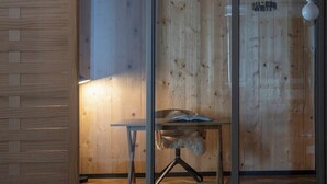 Una stanza con pavimento in legno, un divisorio in vetro, un tavolo con lampada a sospensione e un lampadario.