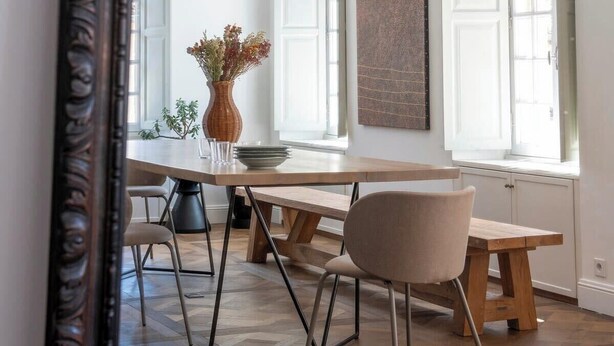 Zona pranzo con tavolo in legno, sedie, un vaso con fiori e un lampadario moderno.