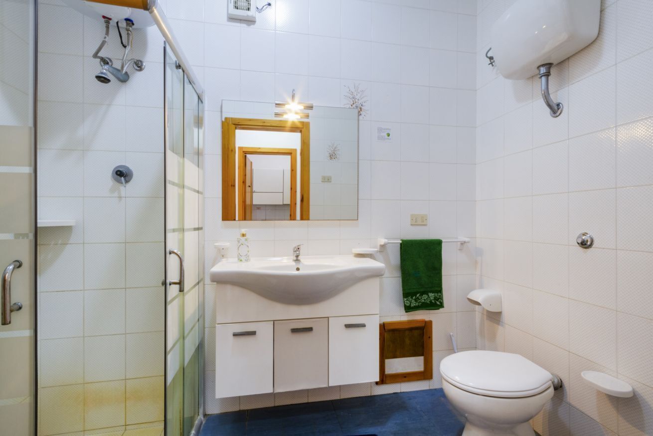 Un baño con ducha, lavamanos, espejo, inodoro y un taburete de madera.