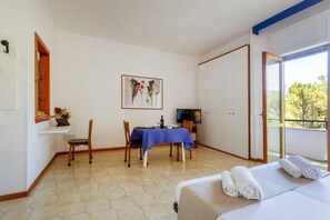 A room with a bed, a dining table with chairs, a TV, and a painting on the wall. - A cozy studio apartment with a balcony and kitchenette—perfect for two—located within the Campoverde Residence in Vernole, set in a Mediterranean pine forest between San Cataldo and the Le Cesine Nature Reserve. The property is just a short distance  (Campo Verde)