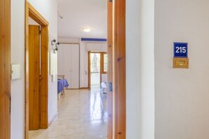 A hallway with wooden doors, a blue sign with the number 215, and a view into a room with a bed and a window. - A cozy studio apartment with a balcony and kitchenette—perfect for two—located within the Campoverde Residence in Vernole, set in a Mediterranean pine forest between San Cataldo and the Le Cesine Nature Reserve. The property is just a short distance  (Campo Verde)