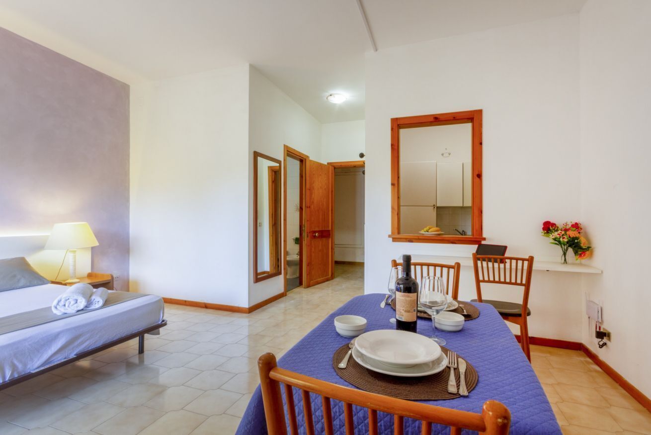 Une chambre d’hôtel avec un lit, une table à manger dressée pour deux personnes, un miroir et un petit bureau avec une chaise.
