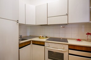 A kitchen with white cabinets, a stainless steel sink, a built-in oven, and a countertop with a kettle and a red container. - A cozy studio apartment with a balcony and kitchenette—perfect for two—located within the Campoverde Residence in Vernole, set in a Mediterranean pine forest between San Cataldo and the Le Cesine Nature Reserve. The property is just a short distance  (Campo Verde)
