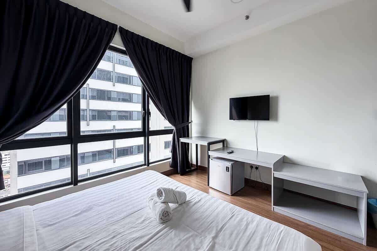 A hotel room with a bed, desk, TV, and large windows.