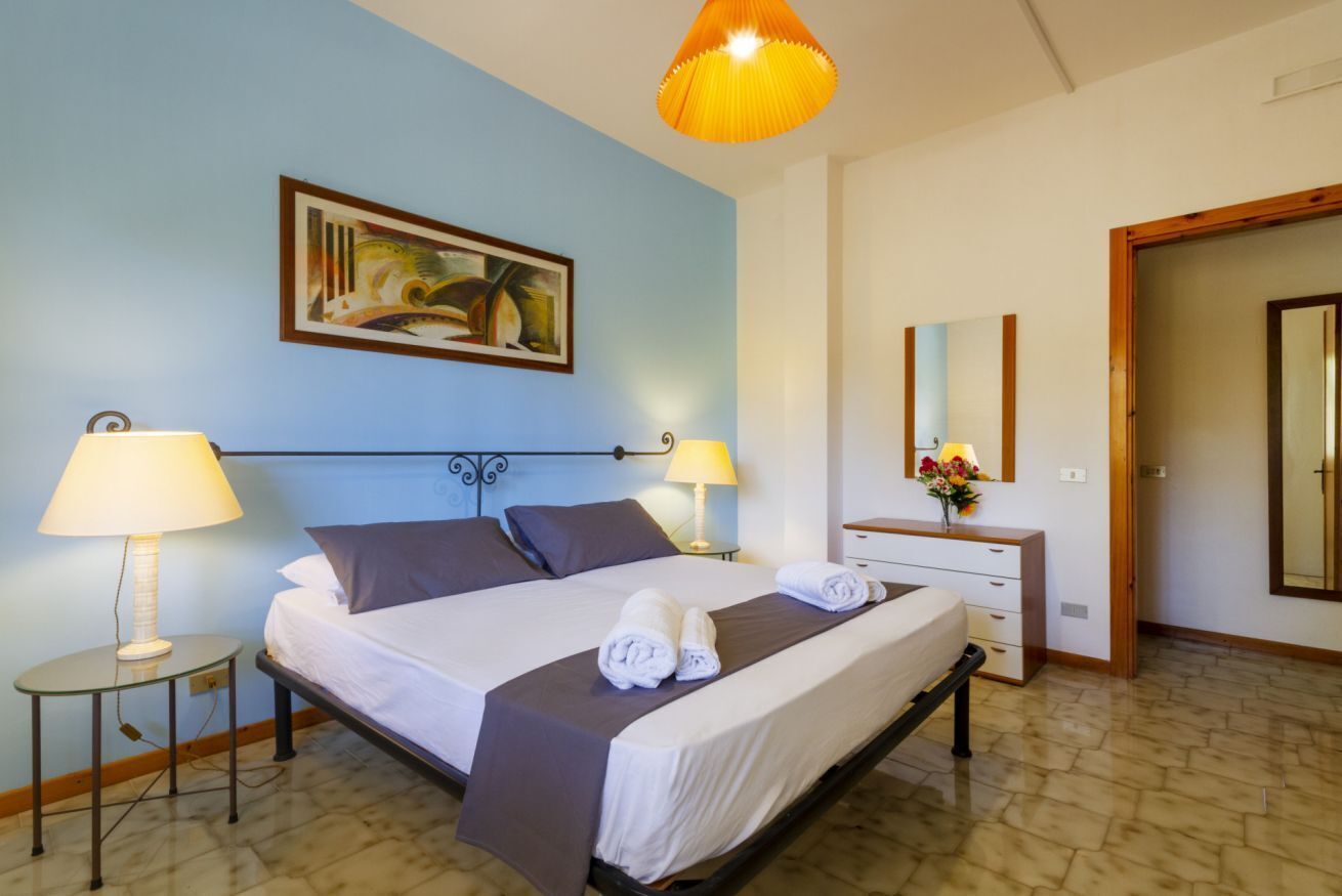A hotel room with a bed, two bedside lamps, a painting on the wall, a dresser, and a mirror.