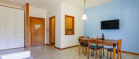 A room with a dining table, chairs, a television mounted on the wall, and a wardrobe.