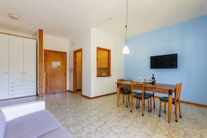 Ein Zimmer mit Esstisch, Stühlen, einem an der Wand befestigten Fernseher und einem Kleiderschrank.