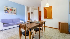 A dining area with a wooden table, chairs, a white sofa, and a painting on the wall. - A delightful apartment with a balcony that sleeps up to four people, located within the Campoverde Residence in Vernole—set in a Mediterranean pine forest between San Cataldo and the Le Cesine Nature Reserve. The property is just a short distance from  (Campo Verde)