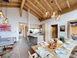 A modern kitchen with wooden beams, a dining area set for a meal, and a living room with a sofa. - The Fustic Apartment—Accommodates 8 People—Near the Slopes (Les Gets)