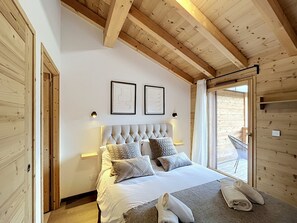 Ein Schlafzimmer mit Holzboden, einem großen Bett mit vielen Kissen, zwei Wandleuchten und einer Glastür, die nach draußen führt.