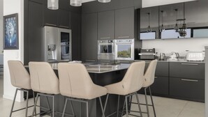 Une cuisine moderne dotée d’un îlot central, de tabourets de bar, d’appareils électroménagers en acier inoxydable et de luminaires suspendus.