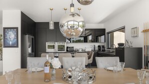 Une salle à manger moderne avec une table en bois dressée pour six personnes, un grand miroir et une cuisine en arrière-plan.